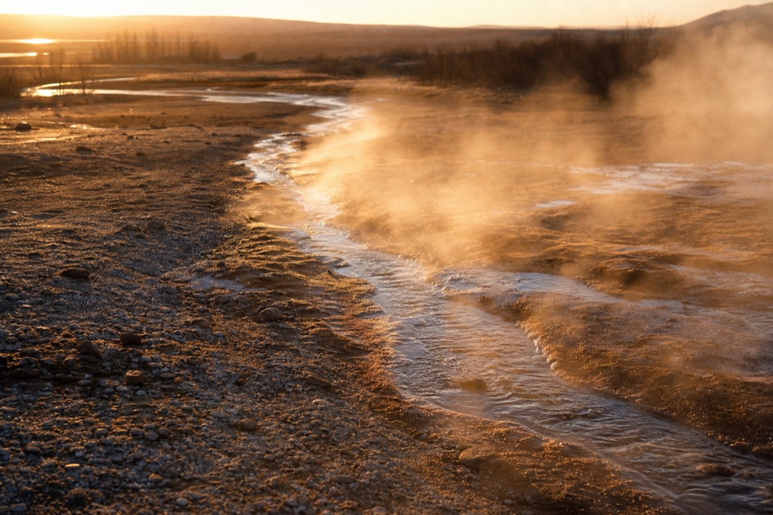 Steaming runoff channel crossing pale mineral gravel at Geysir in low evening light