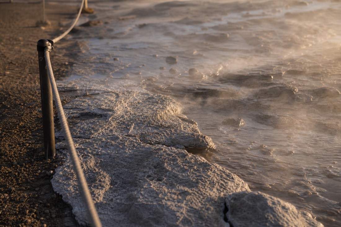 Cracked mineral sinter crust and steaming ground beside a marked path at the Geysir geothermal area