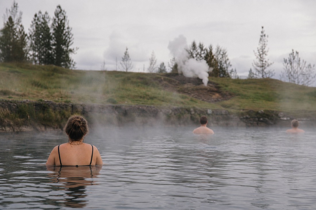 Bathers relaxing in the steaming warm water of the Secret Lagoon at Flúðir with an old stone rim and grass around it
