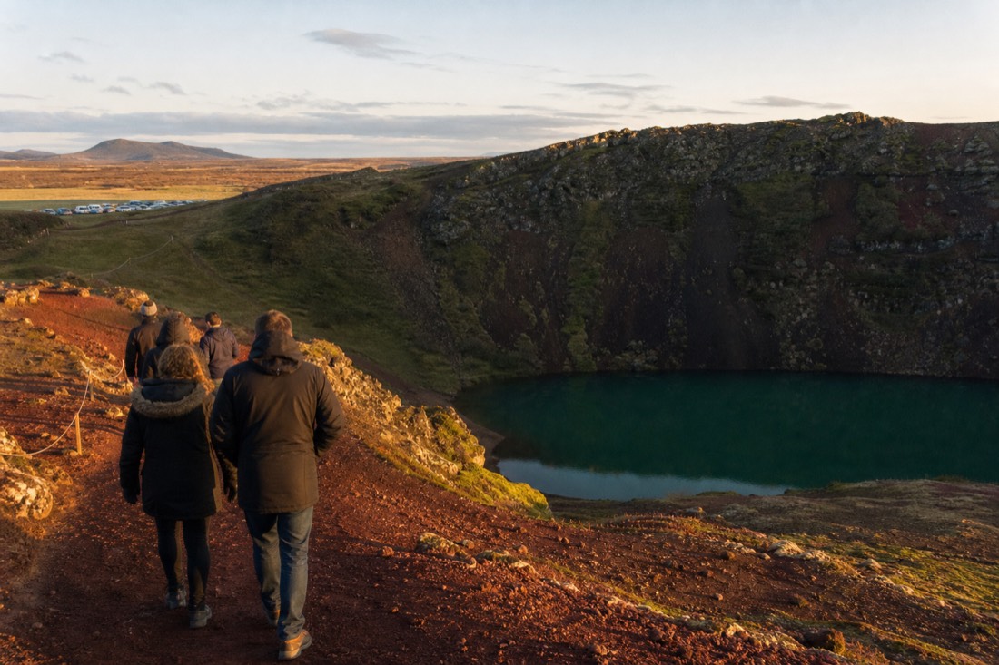 Walkers on the red volcanic rim of Kerið crater above its blue-green lake
