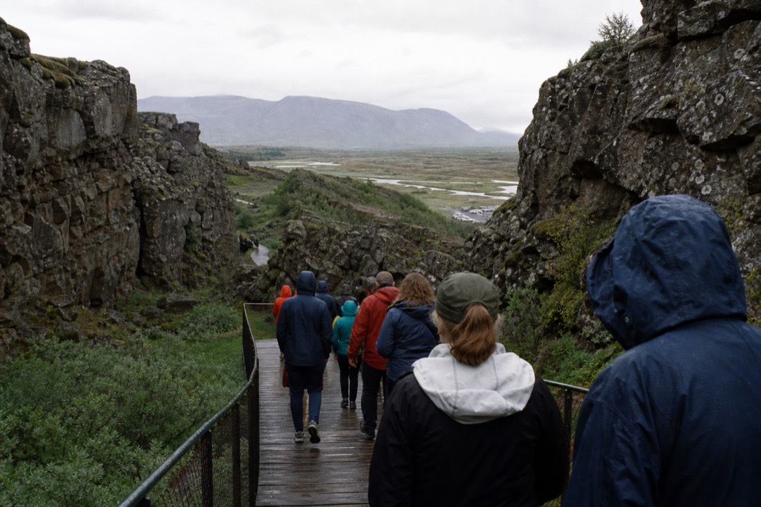 Tour group seen from behind walking the wooden boardwalk down into the Almannagjá gorge at Þingvellir