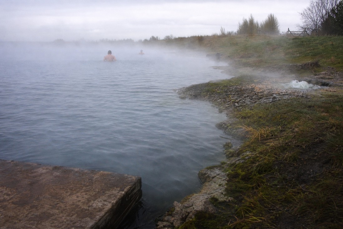 Steam rising off the Secret Lagoon pool at Flúðir with mossy geothermal vents along the grassy bank