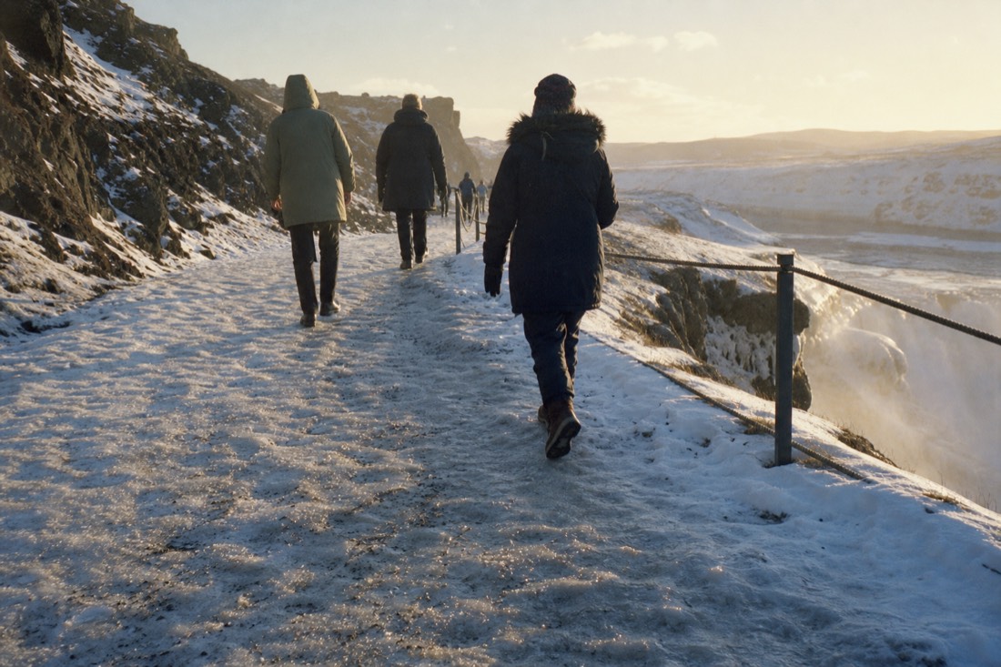 Visitors picking their way along an icy snow-covered path near the Gullfoss viewpoint, seen from behind