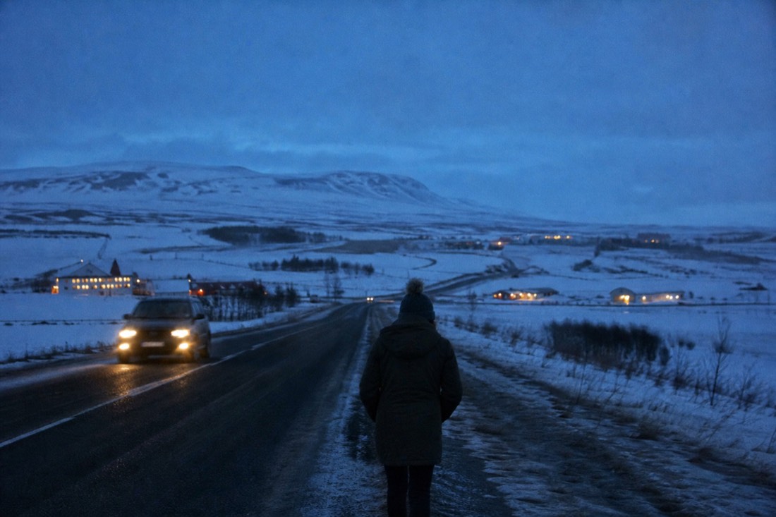 Snow-covered farm and road near Laugarvatn at deep blue winter dusk, farm lights glowing across the fields