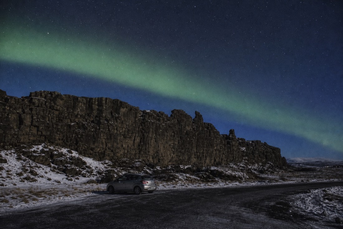 Green aurora over the Þingvellir rift on a clear cold night with a single parked car below