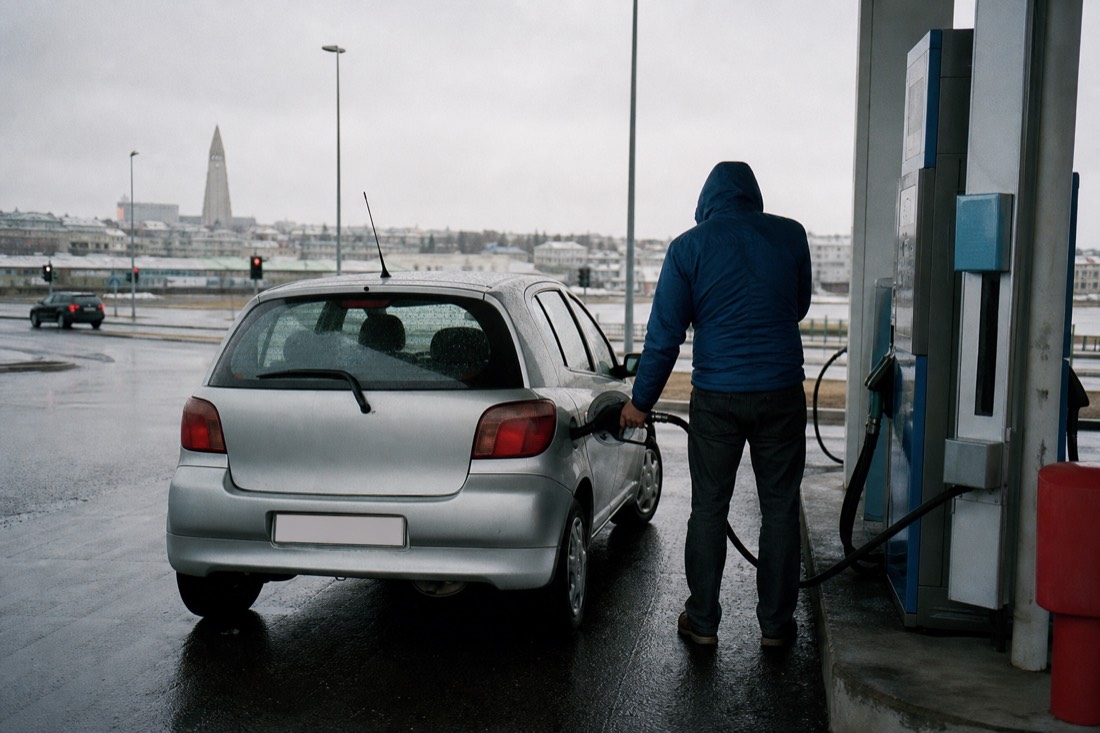 A traveller filling a small unbranded rental hatchback at a self-service fuel pump on a wet Reykjavík forecourt