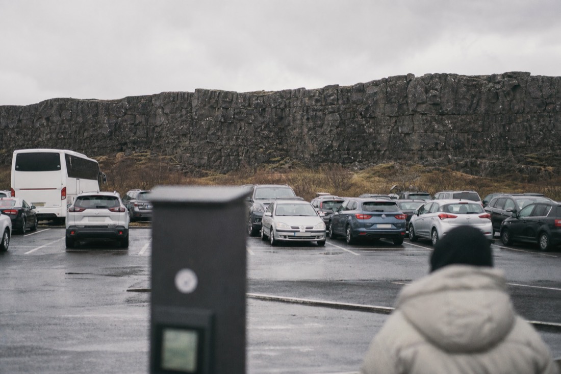 Rental cars and a tour coach parked at the Þingvellir P1 car park with the Almannagjá rift behind