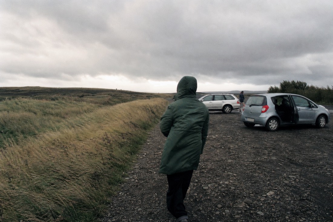 Strong wind flattening grass at an exposed roadside car park near Gullfoss under grey afternoon light