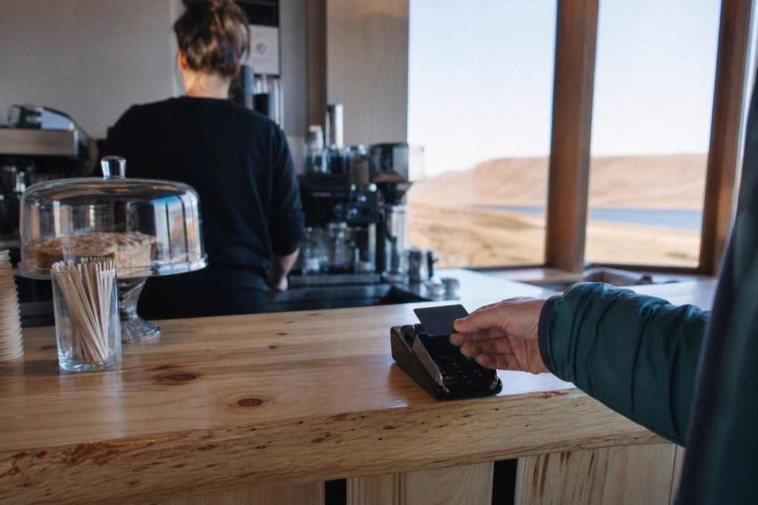 A traveller paying by contactless card at a small café counter in Laugarvatn on a bright afternoon