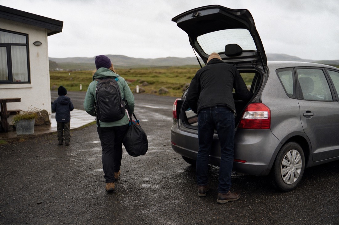 A family loading a small hatchback outside a guesthouse near Selfoss on an overcast morning