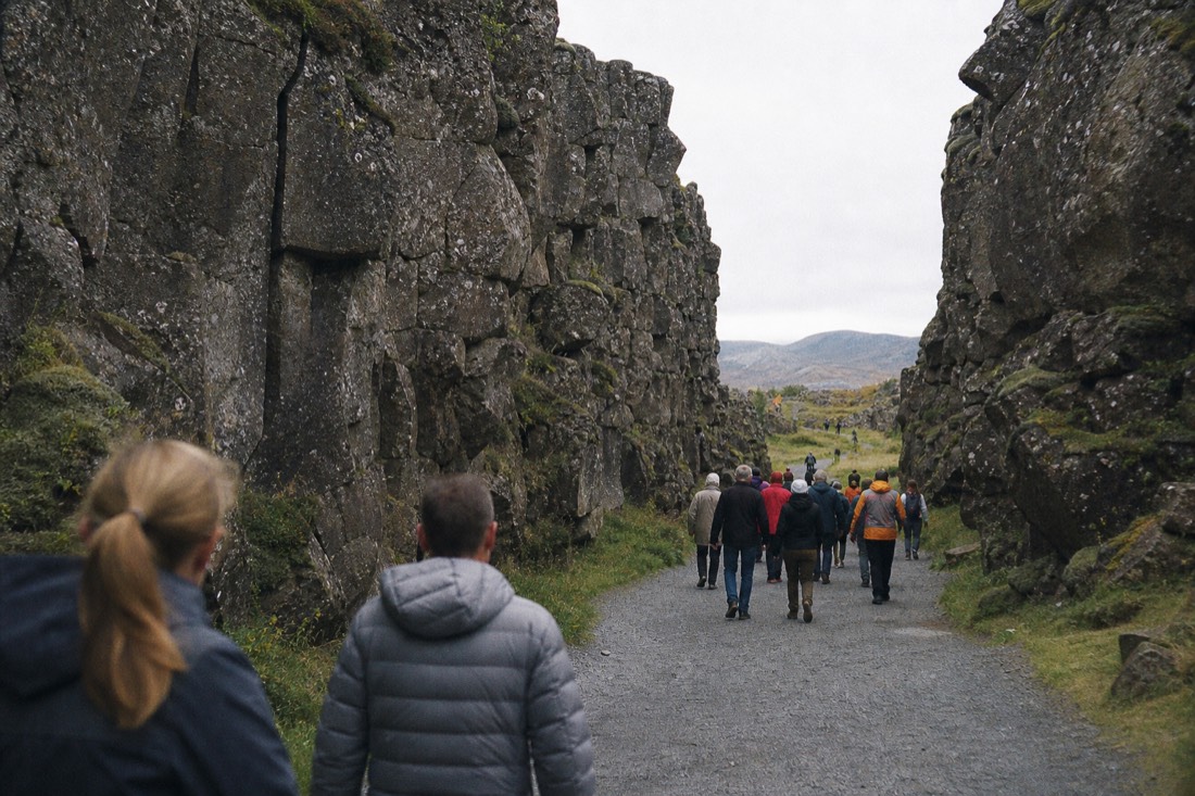 Tour groups walking the Almannagjá gorge path at Þingvellir under flat noon cloud
