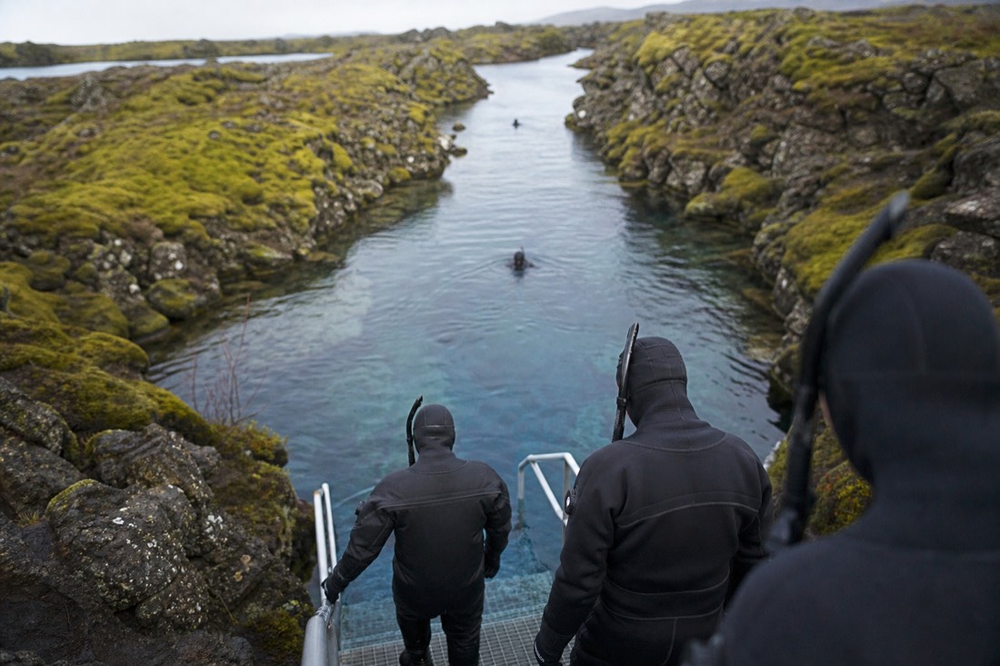 Snorkelers in dry suits at the edge of the clear glacial water of Silfra fissure at Þingvellir