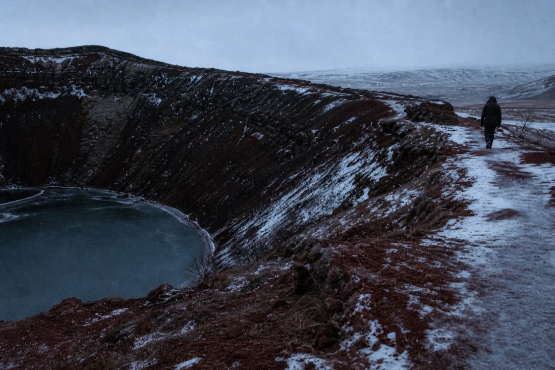Rim path around the red volcanic slopes of Kerið crater at winter dusk