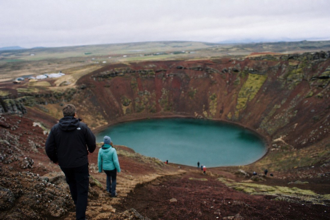 Red volcanic slopes and the blue-green lake inside Kerið crater under an overcast sky