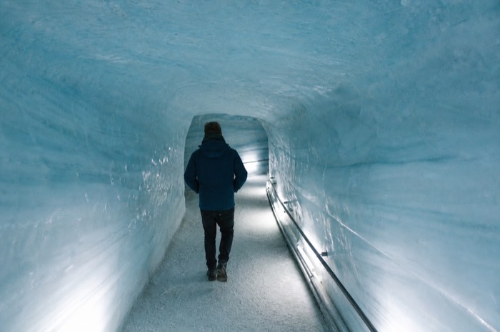 Person walking through a blue-lit man-made ice tunnel deep inside Langjokull glacier