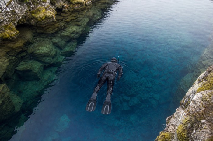 Snorkeler in a drysuit floating over the vivid blue water of the Silfra fissure between tectonic plates at Thingvellir