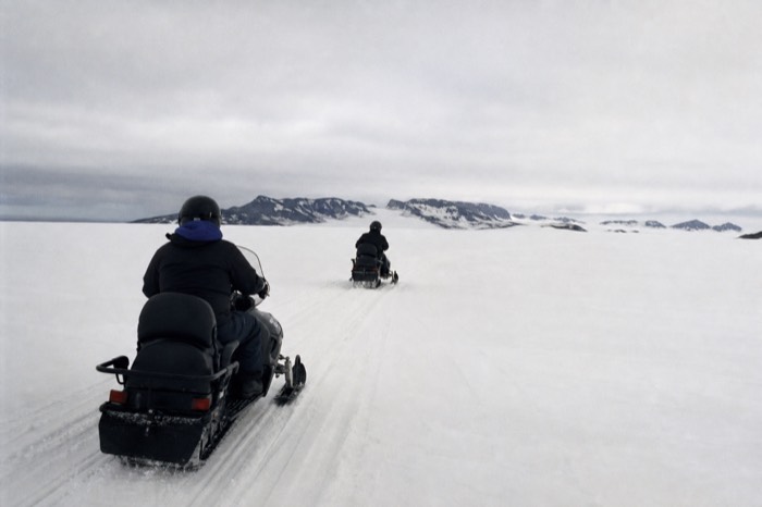 Two snowmobilers crossing the white expanse of Langjokull glacier under an overcast Icelandic sky