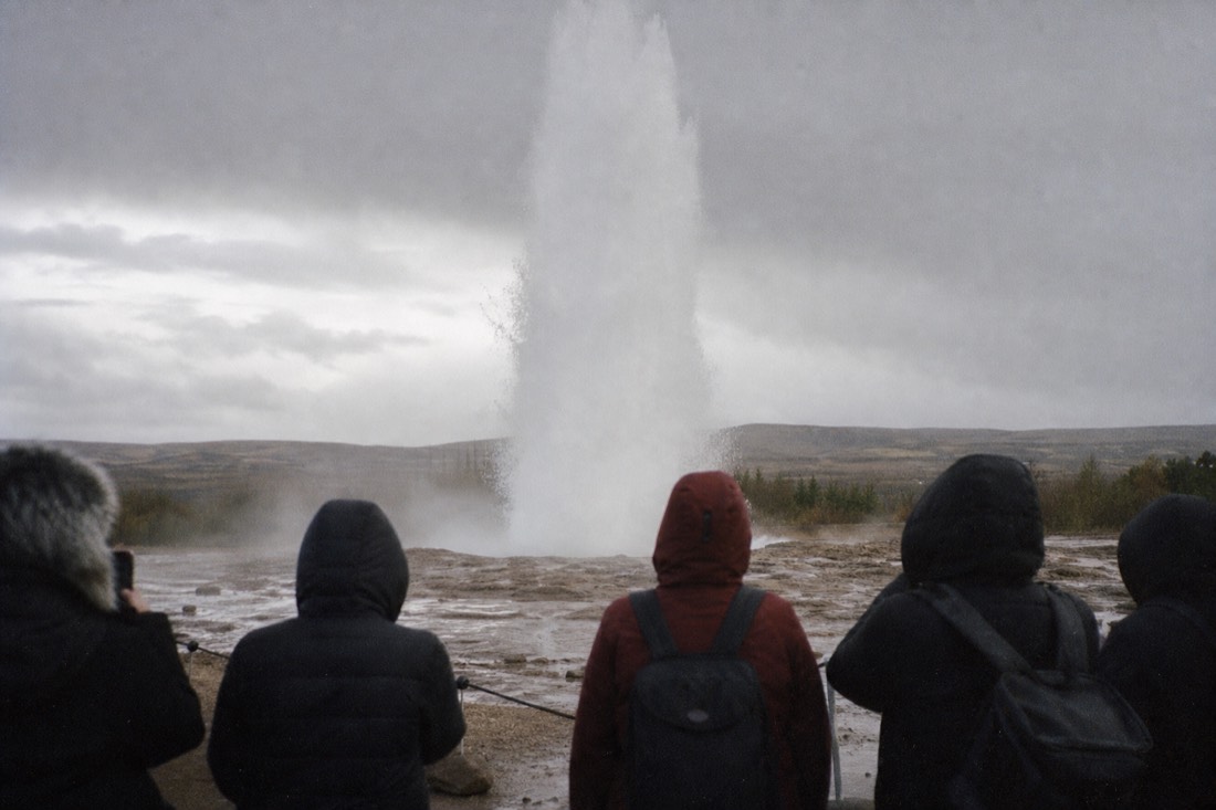 Strokkur geyser mid-eruption at the Geysir geothermal area, water column against grey Icelandic sky